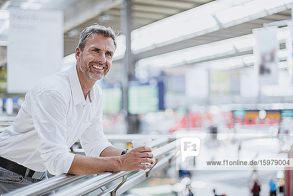 Smiling businessman holding coffee looking away while standing by railing
