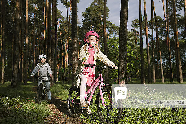 Mädchen und Junge fahren mit dem Fahrrad auf einem Fußweg im Wald