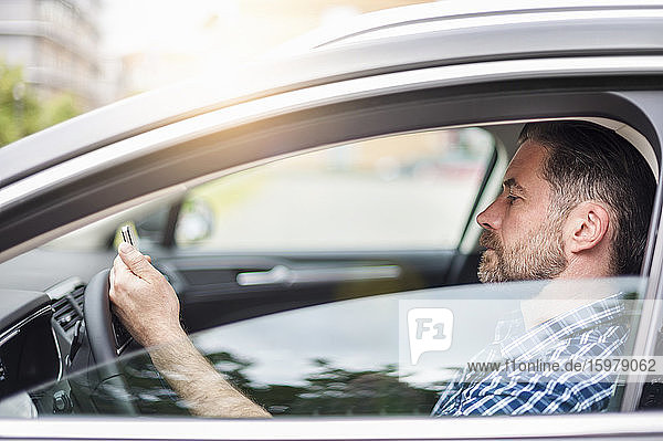 Seitenansicht eines gut aussehenden Mannes  der im Auto sitzend ein Mobiltelefon benutzt