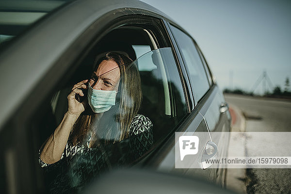 Mittlere erwachsene Frau mit Schutzmaske benutzt Smartphone im Auto