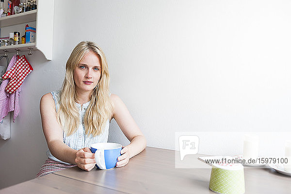 Porträt einer blonden jungen Frau  die am Tisch in der Küche sitzt