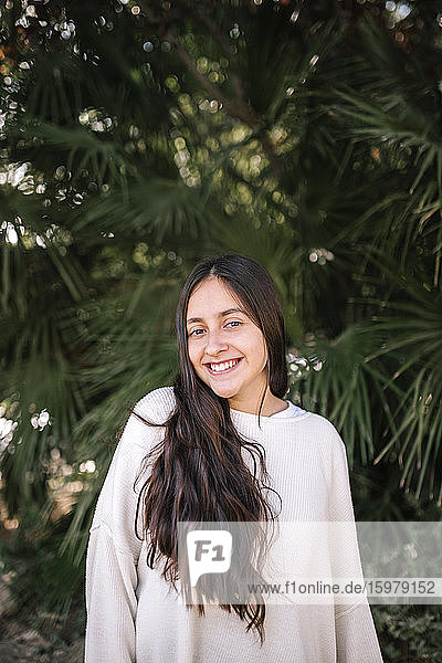 Portrait of smiling teenage girl standing against palm tree at park
