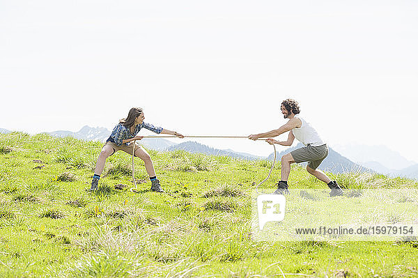 Mid adult couple pulling rope while competing in tug-of-war on mountain against clear sky