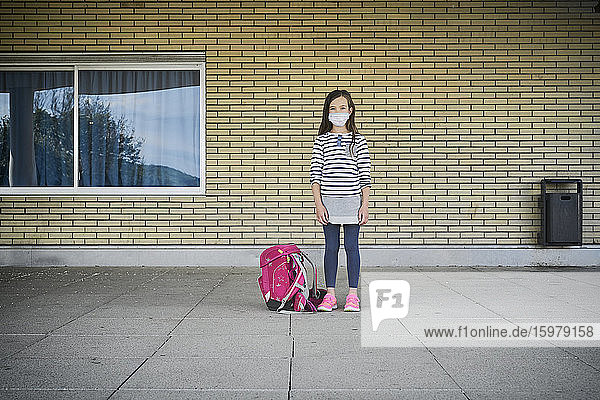 Girl with schoolbag wearing mask standing in front of building
