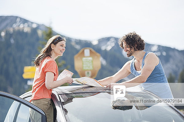 Lächelndes erwachsenes Paar mit Landkarte auf dem Autodach während einer Autoreise