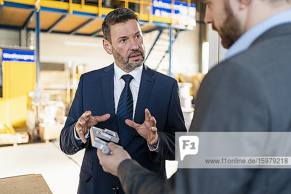 Two businessmen having a meeting in a factory discussing workpiece