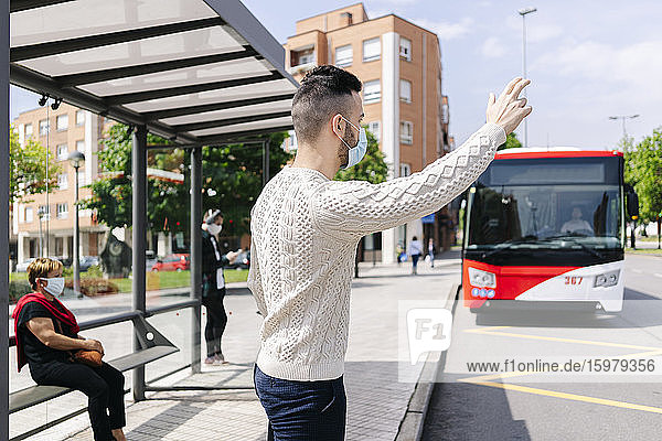 Mann mit Schutzmaske steht an einer Bushaltestelle und ruft ein Taxi  Spanien