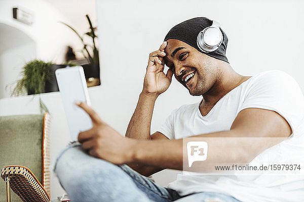 Portrait of smiling man using mini tablet and headphones at home