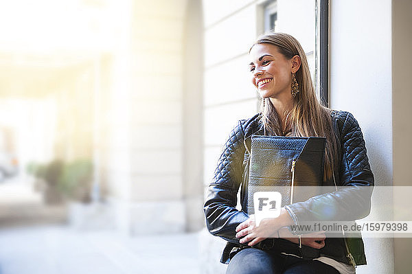 Glückliche junge Frau  die einen Laptop hält und auf der Fensterbank eines Cafés sitzt