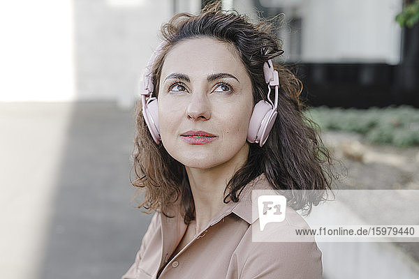 Thoughtful businesswoman listening music through headphones during sunny day