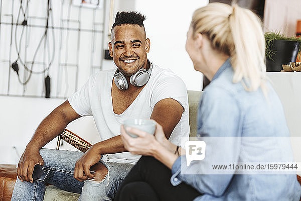 Porträt eines lachenden Mannes mit Kopfhörern und Smartphone zu Hause