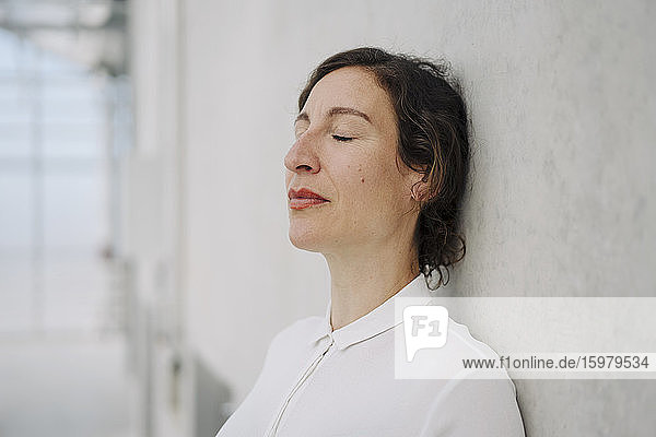 Portrait of a businesswoman with closed eyes leaning against a concrete wall