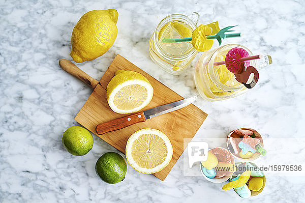 Schneidebrett  Küchenmesser  Zitronen  Limetten  Gummibonbons und Gläser mit frischer  selbstgemachter Limonade
