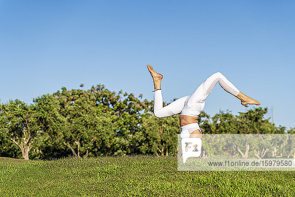 Frau übt Yoga auf Rasen in der Sonne und macht einen Kopfstand