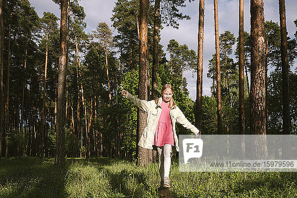 Mädchen geht auf Baumstamm im Wald