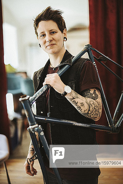 Porträt einer gepiercten und tätowierten Frau mit Fahrradrahmen auf der Schulter