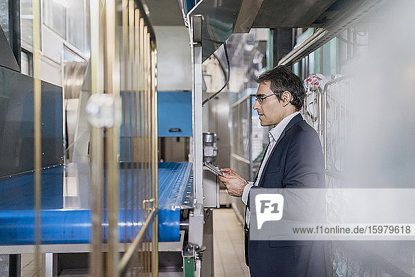 Älterer Geschäftsmann mit Tablette am Fließband in einer Fabrik