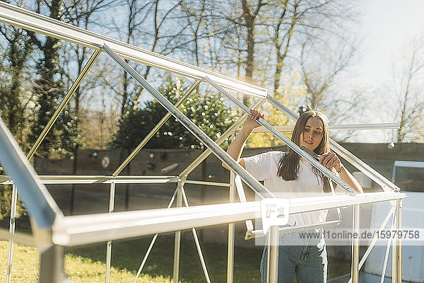 Junge Frau baut Gewächshaus im Garten an einem sonnigen Tag