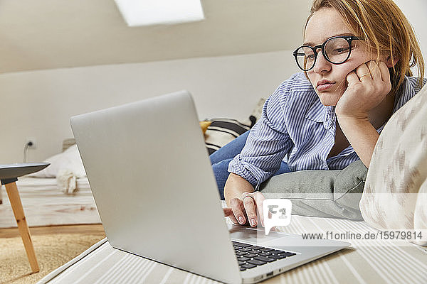 Porträt einer gelangweilten jungen Frau  die zu Hause einen Laptop benutzt