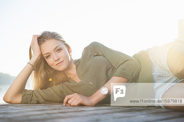 Portrait of smiling young woman lying on jetty at backlight