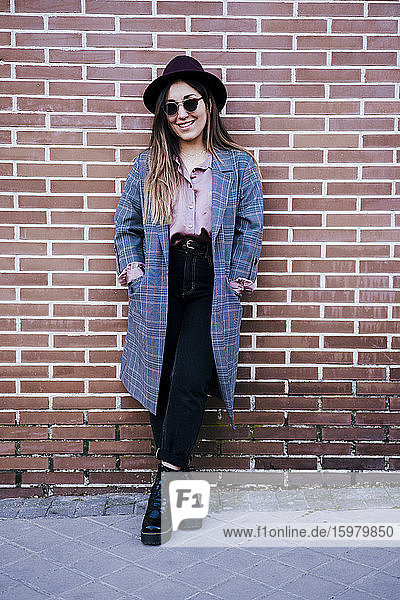Portrait of fashionable woman standing in front of brick wall