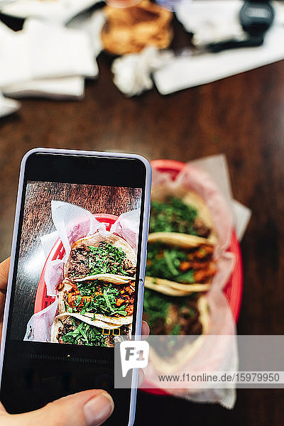 Hand of woman photographing tacos on table with smart phone in restaurant