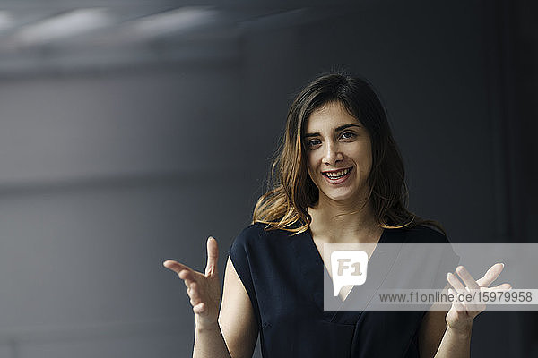 Porträt einer gestikulierenden jungen Geschäftsfrau vor grauem Hintergrund