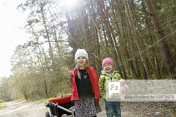 Zwei kleine Schwestern ziehen eine Draisine auf einem Waldweg