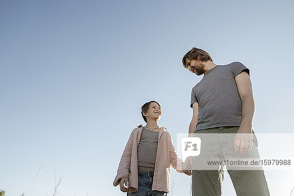 Vater und Tochter halten sich an den Händen  während sie gegen den klaren Himmel im Park stehen