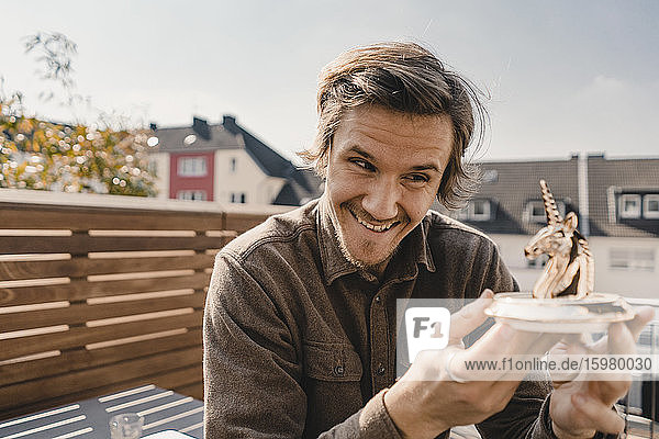 Junger Unternehmer schaut lächelnd auf eine Einhorn-Figur