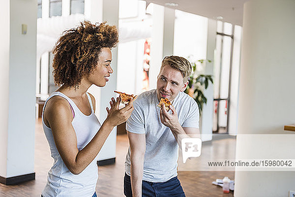 Junge Geschäftsleute essen gemeinsam Pizza zum Mittagessen in einem modernen Büro mit Tischtennisplatte