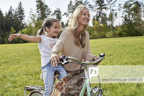 Mädchen mit ausgestreckten Armen genießt Fahrradfahrt mit Mutter auf Pflanzen