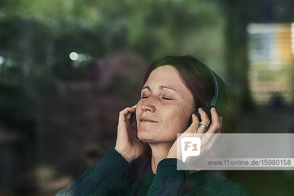 Nahaufnahme einer Frau mit geschlossenen Augen  die zu Hause über Kopfhörer Musik hört