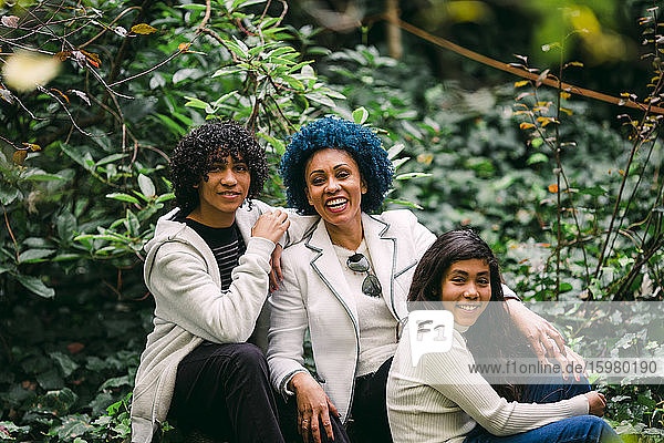 Lächelnde Mutter mit Kindern  die an Pflanzen im Park sitzen