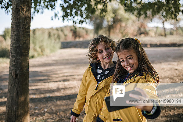 Smiling girl taking selfie with brother from smart phone outdoors