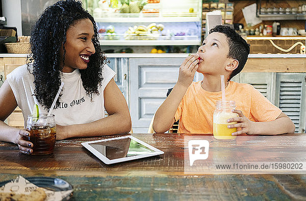 Lächelnde junge Frau sieht ihren Sohn an  der im Restaurant eine Erdbeere isst
