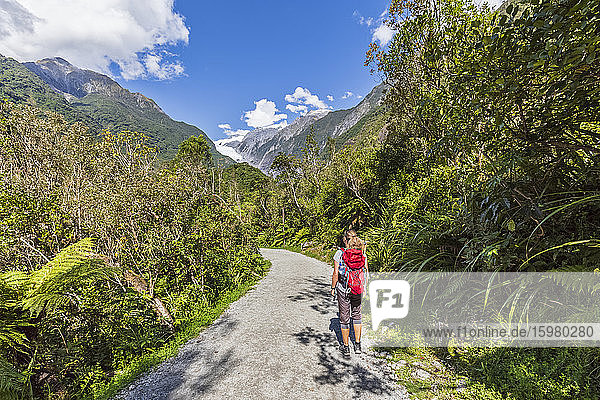 New Zealand  Westland District  Franz Josef  Female backpacker taking break on scenic road leading to Franz Josef Glacier