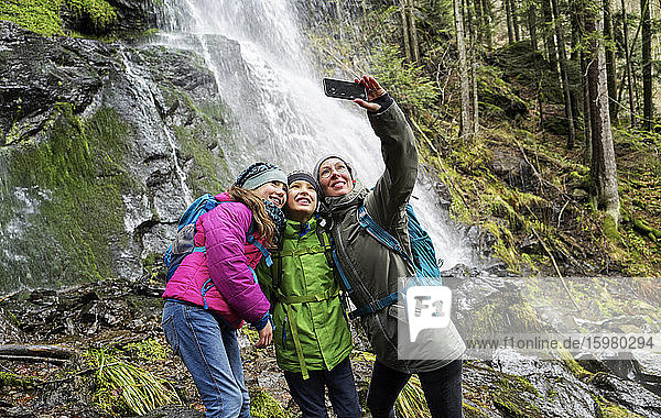 Lächelnde Frau macht Selfie mit Kindern am Zweribach-Wasserfall im Nordschwarzwald