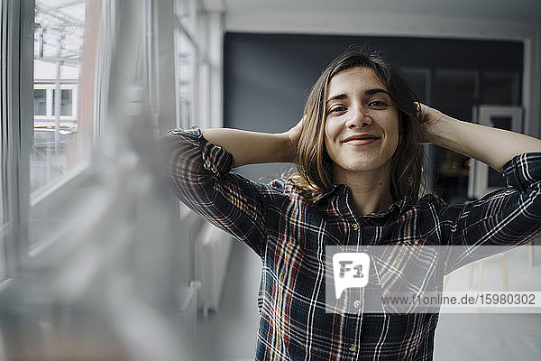 Porträt einer glücklichen jungen Frau mit den Händen hinter dem Kopf in einem Loft