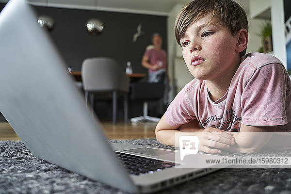 Junge liegt auf dem Boden und arbeitet am Laptop