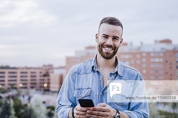 Porträt eines entspannten jungen Mannes mit Smartphone im Freien