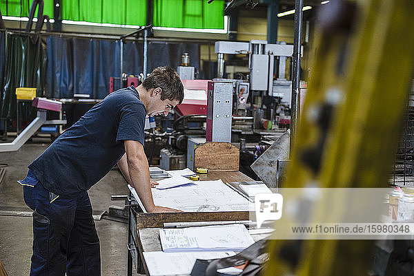 Mann studiert einen Plan auf einer Werkbank in einer Fabrik
