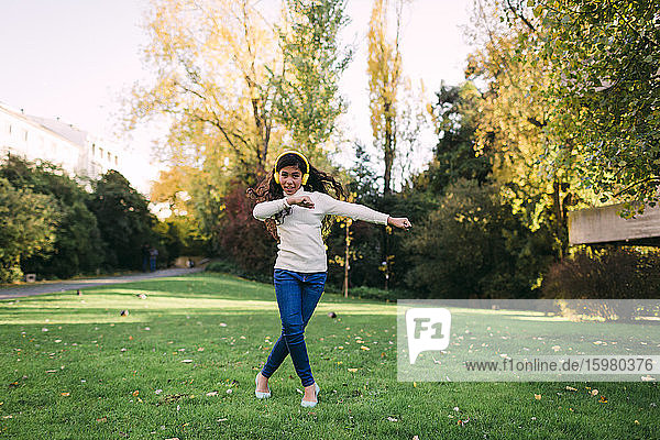 Glückliches Mädchen hört Musik und tanzt auf einer Wiese im Park im Herbst