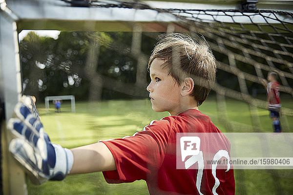 Ernster Junge in Fußballuniform hält Torpfosten auf dem Spielfeld