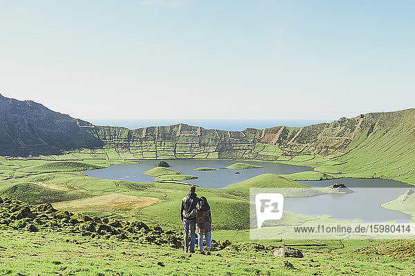 Rear view of couple looking at lake and mountains against clear sky on sunny day  Corvo  Azores  Portugal