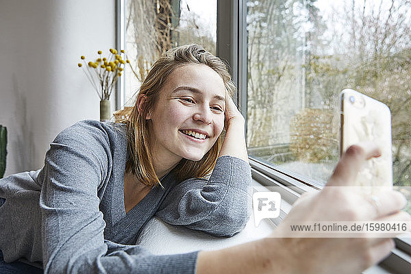 Porträt einer glücklichen jungen Frau  die zu Hause ein Selfie mit ihrem Smartphone macht