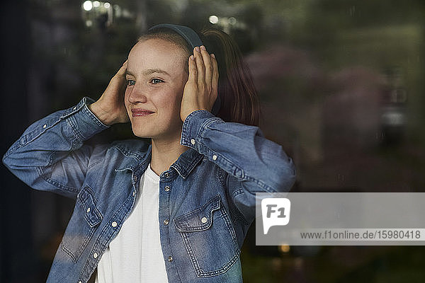 Lächelndes junges Mädchen  das zu Hause über Kopfhörer Musik hört