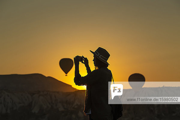 Silhouette einer jungen Frau  die mit ihrem Smartphone fotografiert  während sie an Land in Kappadokien  Türkei  steht