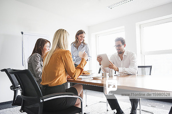 Businessman discussing over digital tablet with female colleagues in board room