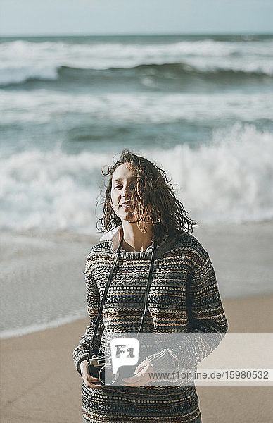 Schöne junge Frau steht mit Kamera am Strand  Praia da Ursa  Lisboa  Portugal